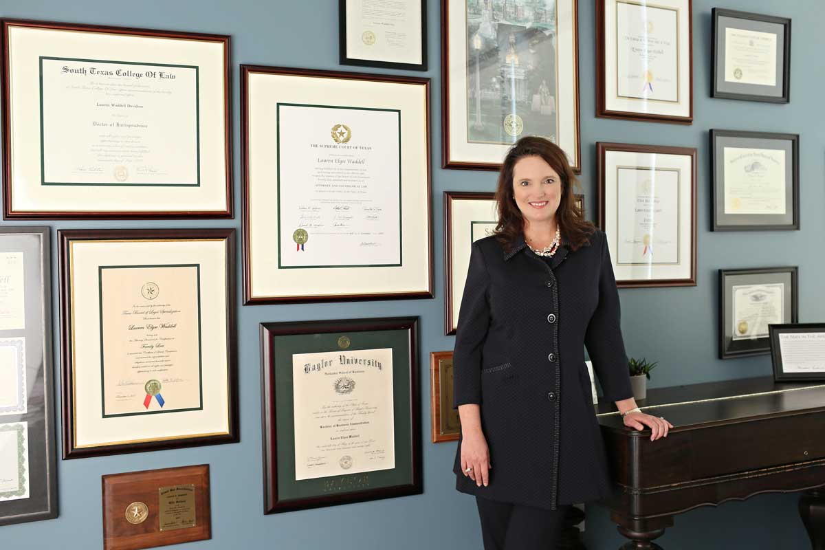 Photo of Lauren E. Waddell standing in front of wall displaying degrees and awards